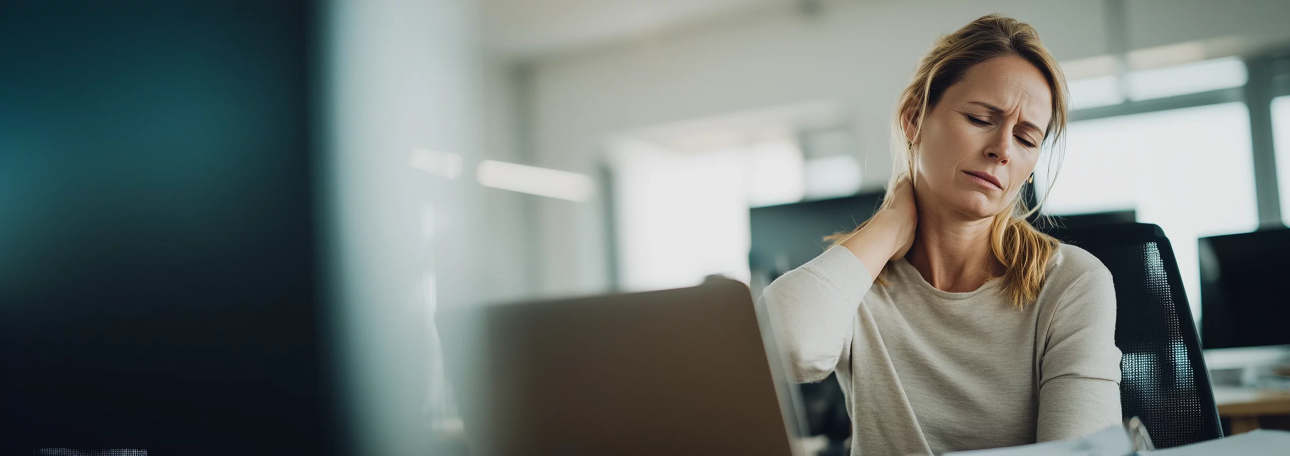 Salariée au bureau ressentant une tension posturale et mentale avant un atelier Yoga ou Pilates au travail.